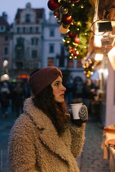 a woman in a fur coat is holding a coffee cup and looking at the street