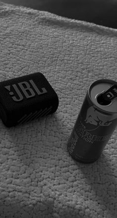 a black and white photo of a can of beer next to a cell phone on a bed