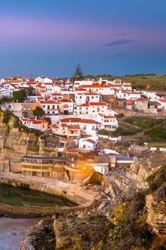 a town on the edge of a cliff with water and cliffs in the foreground