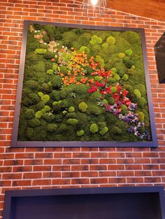 a moss covered wall hanging on the side of a brick building with flowers in it