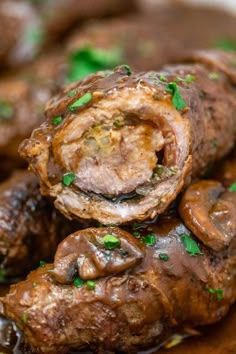 some meat and mushrooms are piled on top of each other in a white bowl with green garnishes