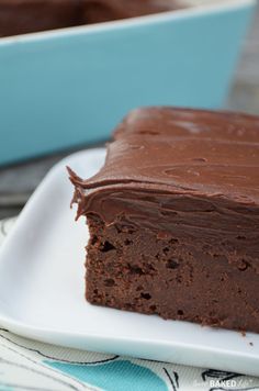 a piece of chocolate cake sitting on top of a white plate next to a blue dish