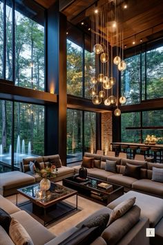 a living room filled with lots of furniture and large windows overlooking the forest outside at night