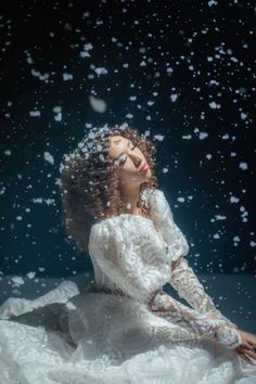 a woman in white dress sitting on the ground with snow falling around her and looking up