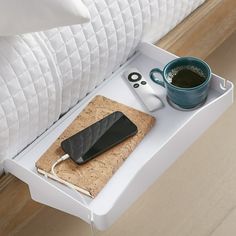 a tray with a coffee cup, cell phone and other items on it next to a bed