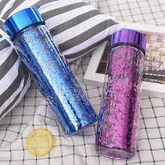 two purple and blue glitter tumblers sitting next to each other on a bed with pillows