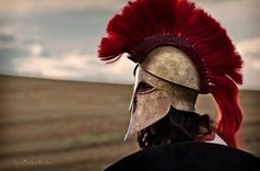 a man wearing a helmet with red feathers on it's head in the middle of a field