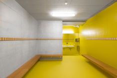 an empty yellow and white bathroom with benches in the hallway next to the sink area