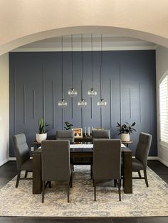 a dining room table with chairs and lights hanging from it's ceiling, in front of a blue wall