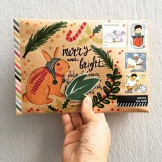 someone is holding up a christmas card with an image of a rabbit and holly wreath on it