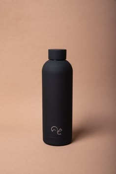 a black water bottle sitting on top of a brown table next to a pink wall