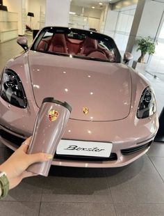 a person is holding the hood up to a pink sports car in a showroom