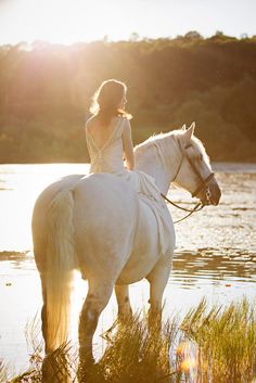 a woman riding on the back of a white horse next to a body of water