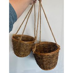 two baskets are hanging from twine rope on the wall, one is holding another