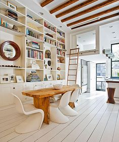 a dining room table with chairs and bookshelves on the wall in front of it