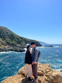 two people standing on rocks near the ocean