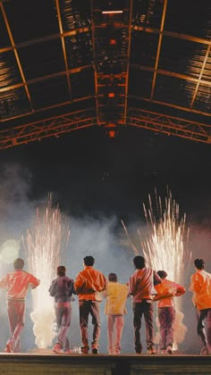 several people standing on a stage with fireworks in the air