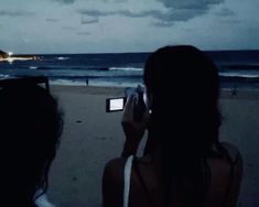 two people on the beach taking pictures with their cell phones at night, and one person holding up a camera