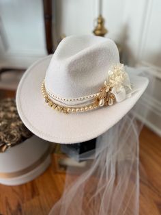 Handmade custom white bridal cowboy hat decorated with beautiful pearly and bling hat bands, rhinestones, letters, and preserved flowers.  This hat can be created with a distressed look, but will closely resemble the images provided. While some cards, ribbons, feathers, and other embellishments may differ slightly, the customizations will remain very similar to those depicted in the photos. Each hat can be shipped in a custom hat box that protects hat shape and features while shipping to you. The hat box is perfect to store your hat in when not worn. Should you choose to ship in a hat box, please add the item to your cart as well. (Price is not included with the purchase of this hat.) If you would like to request additional features or modifications, please do not hesitate to message AD yo Cowboy Hat Veil, Cowboy Hat Decorated, Cowboy Hat With Veil, Bride Cowboy Hat, Embellished Cowboy Hat, Cowboy Hut, Bling Hat, Hat With Veil, Veiled Hats