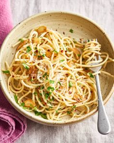 a white bowl filled with pasta and garnished with parsley next to a pink towel