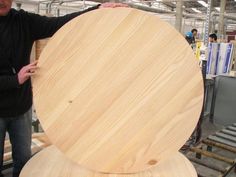 a man standing next to a giant wooden object in a factory with other people working on it