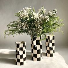 three black and white checkered vases with flowers in them sitting on a table