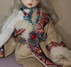 a doll with white hair sitting on top of a bed next to a teddy bear