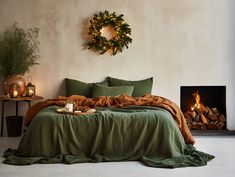 a bed with green sheets and blankets next to a fire place in a room that has a wreath on the wall