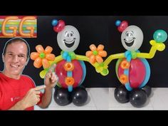 a man standing next to two balloons in the shape of flowers and clowns on top of each other