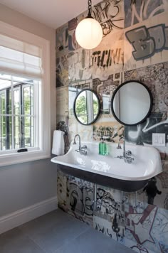 a bathroom with graffiti on the wall and two round mirrors hanging from the ceiling above the sink