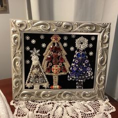 two christmas trees made out of beads in a silver frame on a lace doily