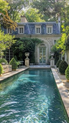 an outdoor swimming pool surrounded by trees and bushes with a house in the back ground