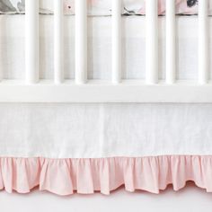 a white crib with pink ruffled bed skirt