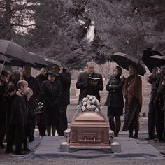 a group of people standing around a casket with umbrellas over it and one person holding an umbrella