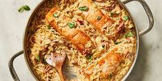 a pan filled with rice and meat on top of a white counter next to a wooden spoon