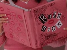 a woman is holding a pink book with the words burn book written in black on it