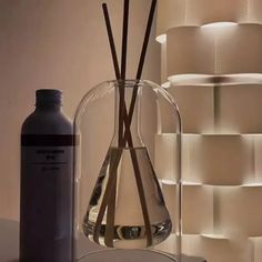 a glass vase with two sticks in it next to a bottle and some lights on the wall