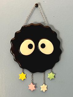 a black clock with two eyes and stars hanging from it's side on a wall