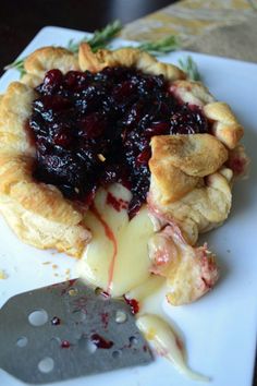 a pie with blueberry sauce and cheese is on a plate next to a knife