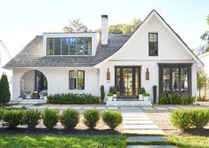 a white house with lots of windows and bushes around it's front yard area