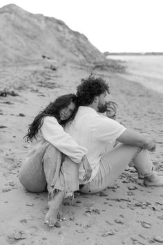 a man and woman are sitting on the beach hugging each other while they both have their arms around each other