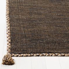 a brown and white rug with tassels on the bottom, sitting on a wooden floor