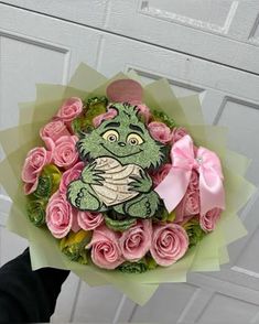 a person holding a bouquet of pink roses with a frog on it's face