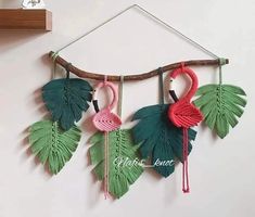 three flamingos are hanging from a branch with green leaves and red yarn on it