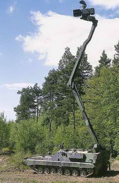 an army vehicle is being lifted by a crane in the middle of a wooded area