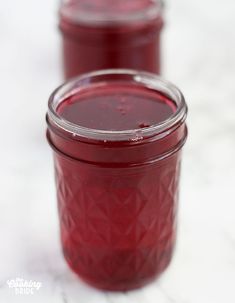 two jars filled with red liquid sitting on top of a white countertop next to each other