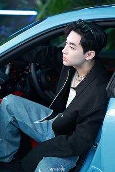 a young man sitting in the driver's seat of a blue car wearing headphones