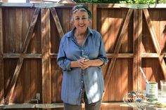 an older woman standing in front of a wooden fence and holding a jar with something on it