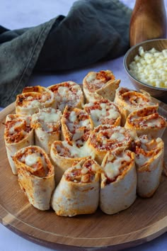 a wooden plate topped with lots of food next to a bowl filled with macaroni and cheese