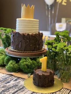 a cake with a candle on it sitting on a table next to other cakes and greenery